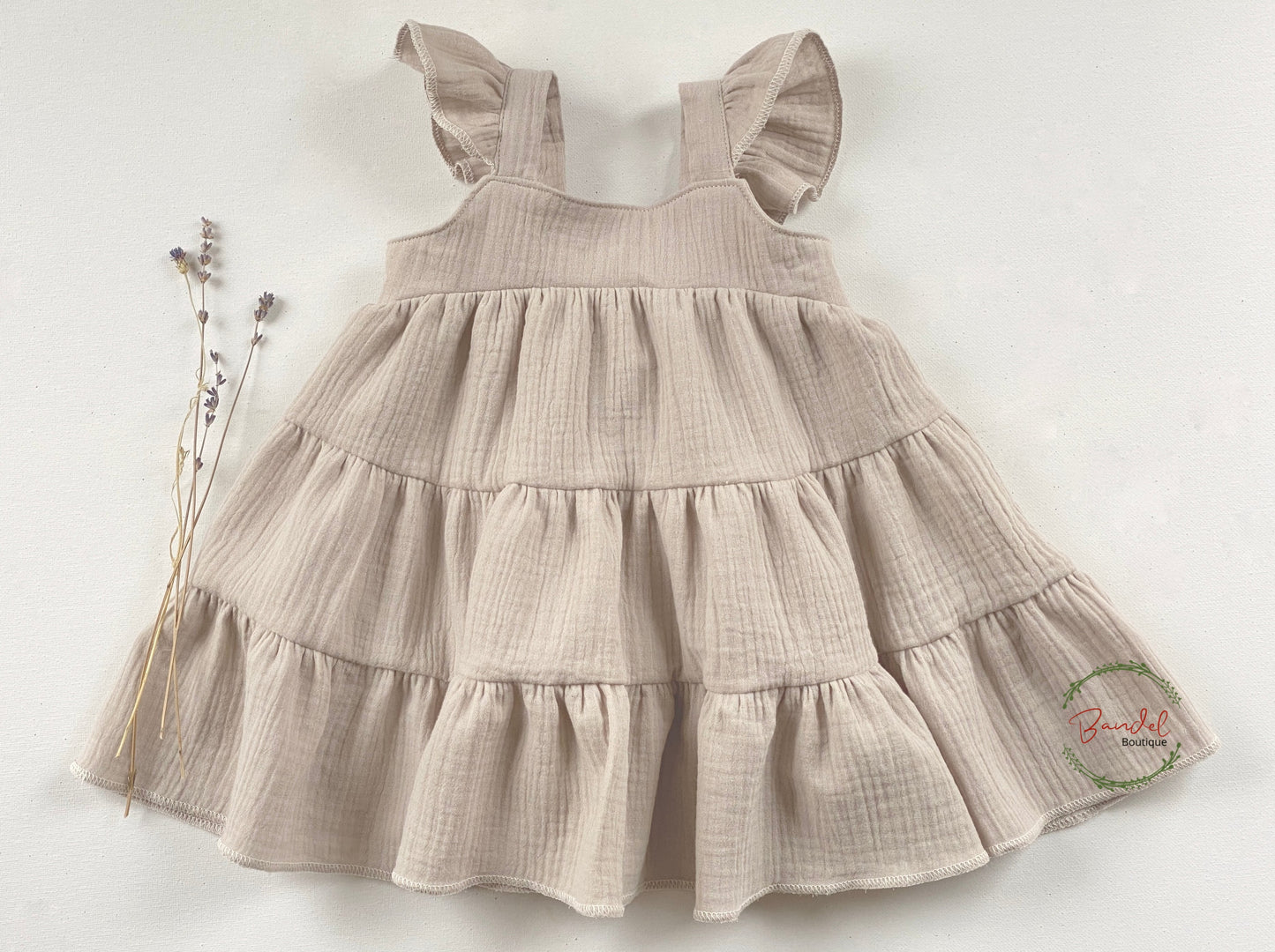 Sand-brown double gauze girl dress is crafted from sustainable fabric. Featuring gathering on the skirt, flutter sleeves, and elastic on the back bodice, this dress offers a comfortable fit and a stylish, timeless look.