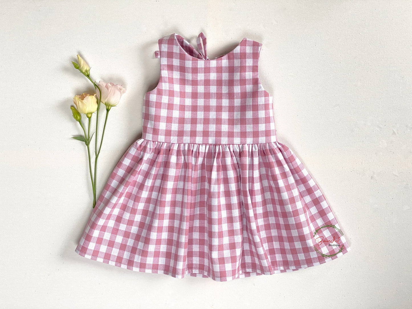 classic Rose Gingham Dress is made from old rose check cotton and features a simple front bodice with two rows of elastic for comfort and ease of fit. The large back opening with a bow-tie gives it a timeless look, perfect for any occasion. Knee length and full skirt provide the perfect balance.