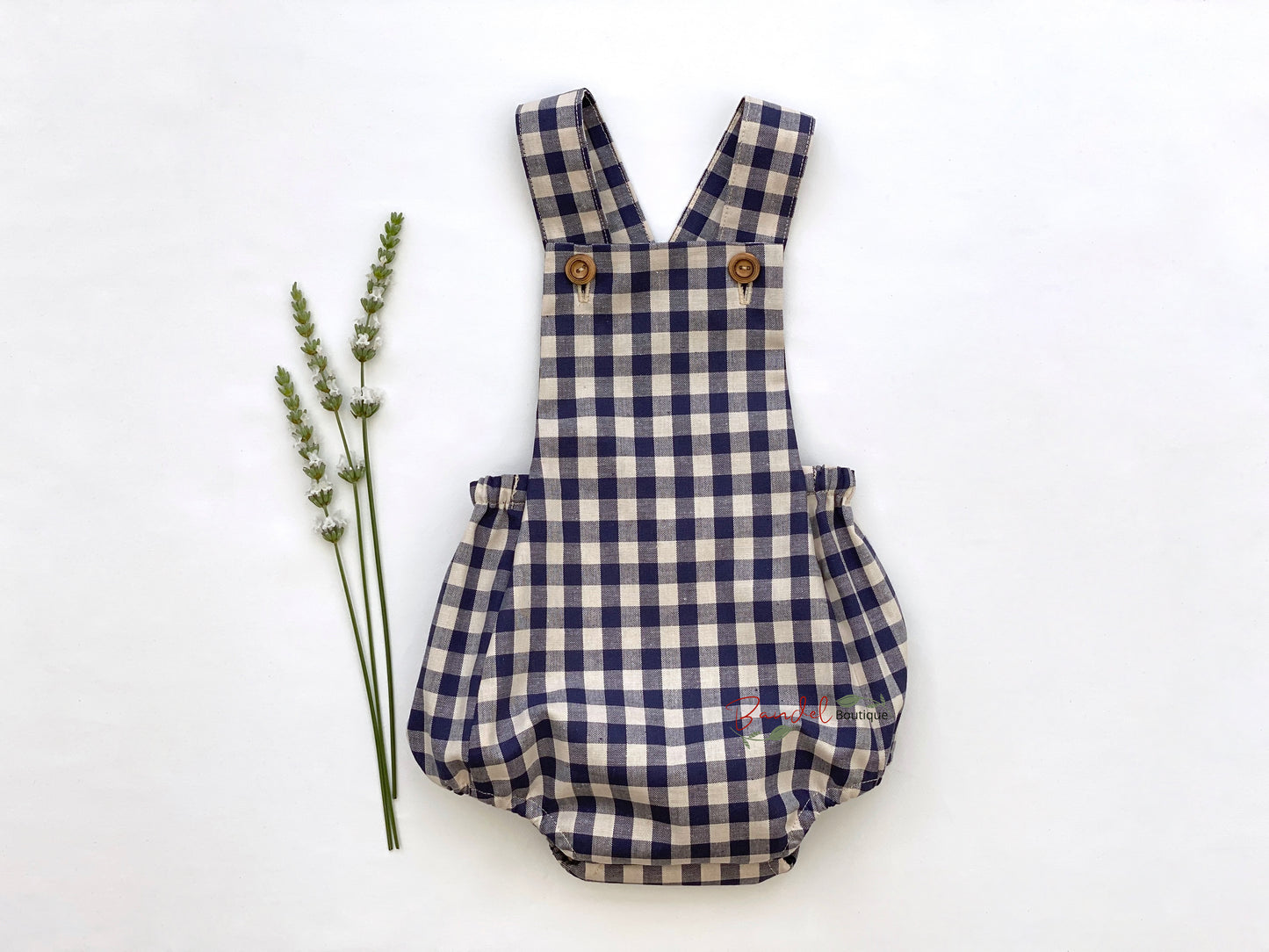 Adorable blue gingham baby romper featuring adjustable straps and rustic wooden buttons. 