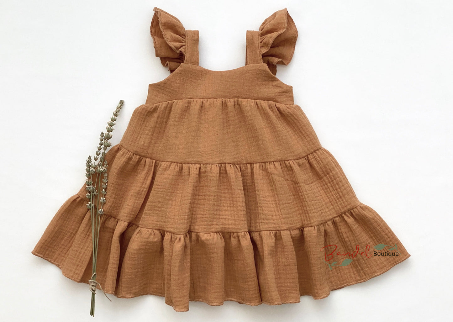 Caramel Flutter Sleeve Girl Dress is crafted from sustainable muslin fabric and features a gathered, tiered skirt and fluttery sleeves. Elastic on the back bodice allows for a comfortable fit.