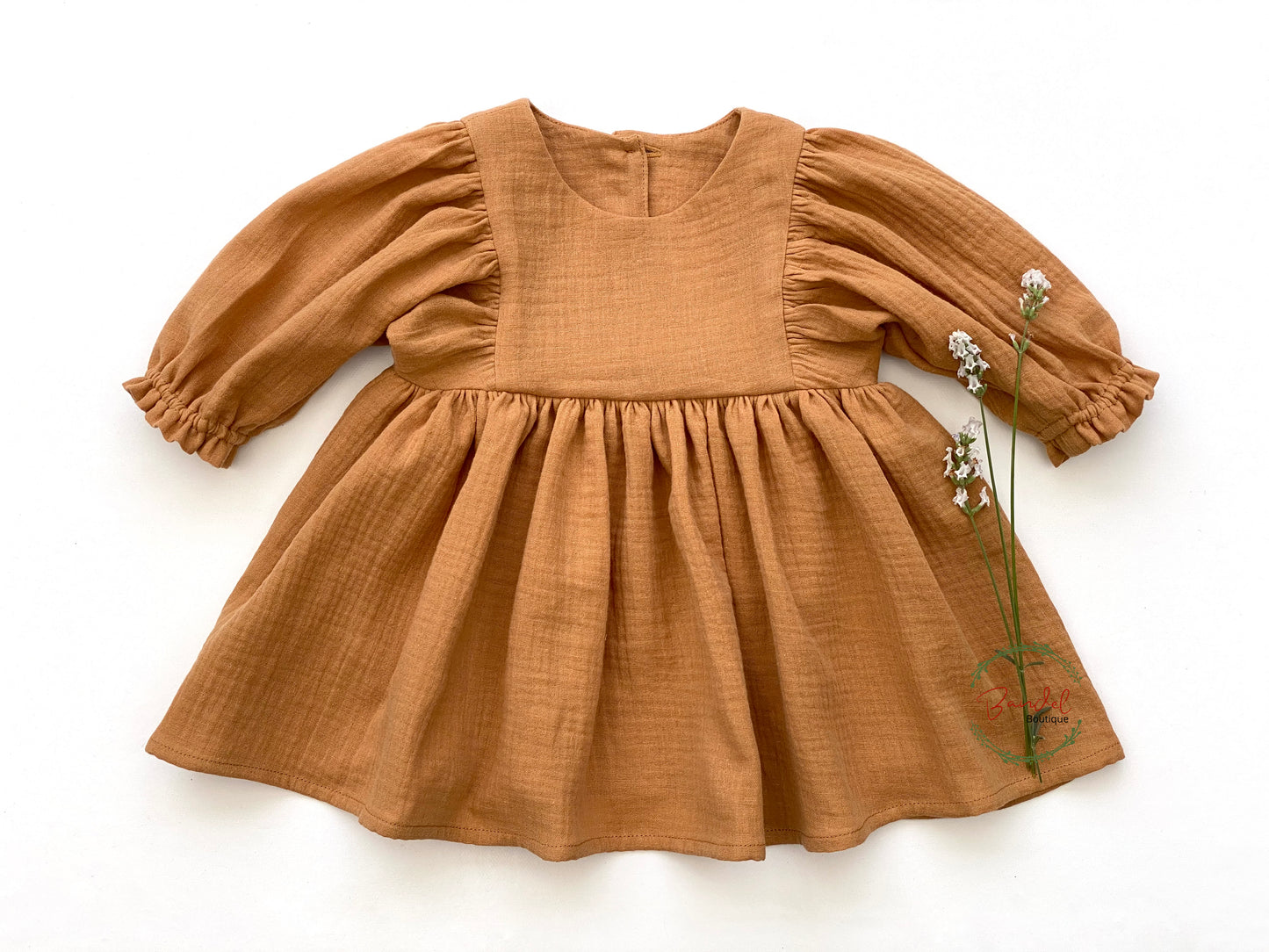 This charming, organic muslin dress is sure to impress! Its caramel-brown hue is perfect for everyday wear and the whimsical style, with its 3/4 length sleeves and ruffled hem with elastic casing, make this knee-length dress a must-have. A wooden button closure in the back completes the look.