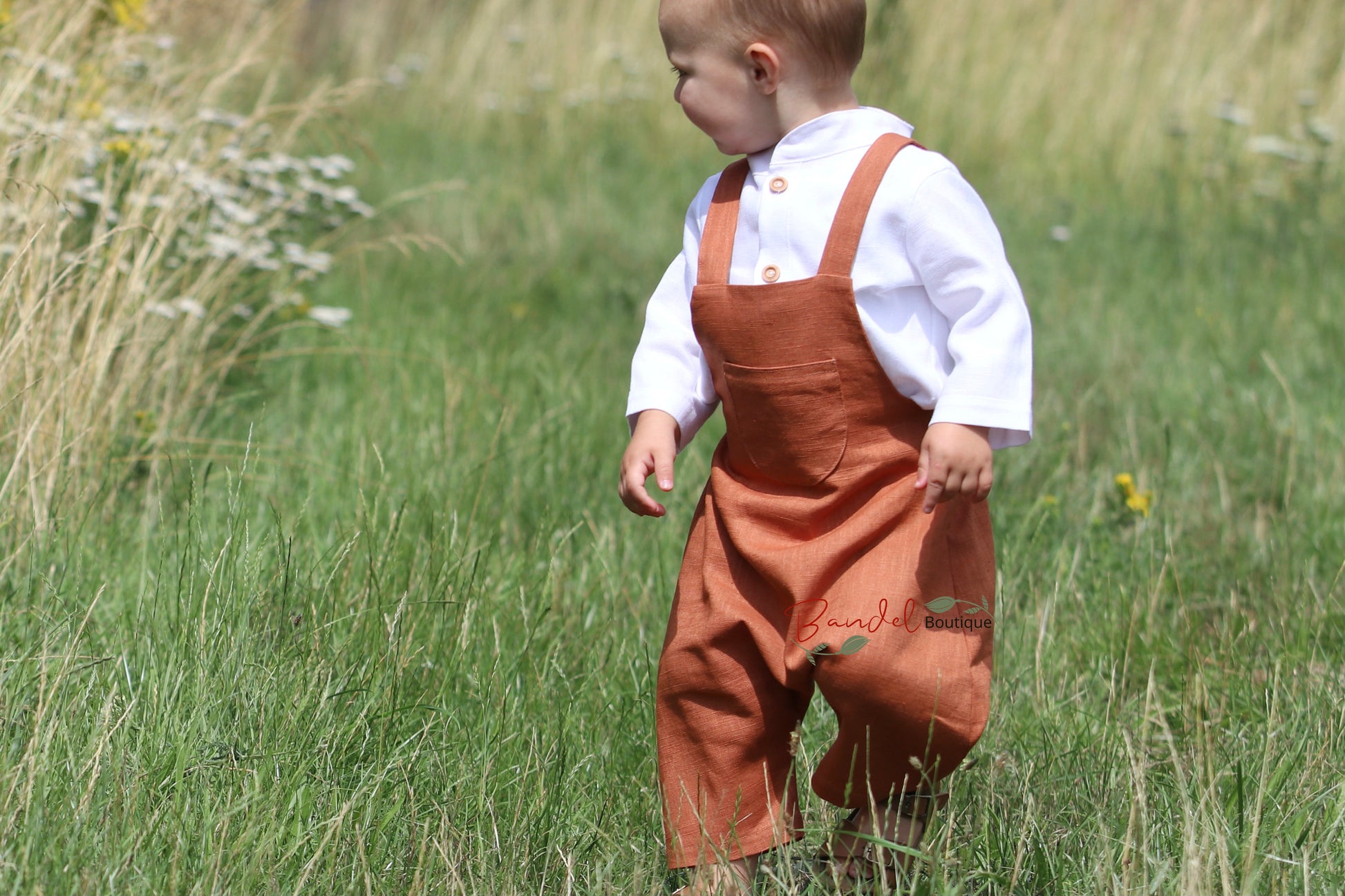 Rust Linen baby romper dungarees feature 3/4 length shorts with a traditional curved front pocket. The elastic back waistband and adjustable tie straps provide a secure fit, and the wooden button closure at the back creates a stylish look.
