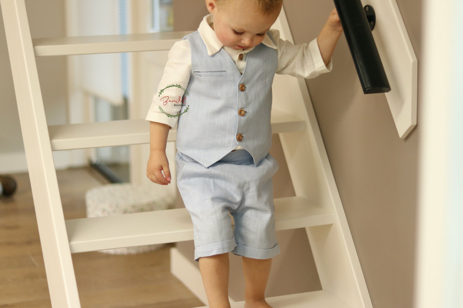 Baby-Blue Short Pageboy Outfit is perfect for your little one. It features a vest with wooden buttons and welt pocket, a shirt with a collar and 3/4 sleeves, and shorts with two side pockets and an elasticized back waistband. Your baby will be comfortable and stylish in this ensemble.
